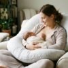 New mother breastfeeding her newborn baby while using a U-shaped pregnancy pillow as nursing support